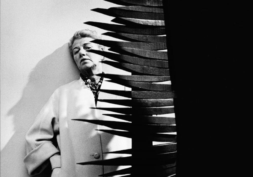 Peggy Guggenheim im weißen Mantel auf einer Ausstellung des Brooklyn Museum of Art Ende der 50er Jahre. Vor ihr steht eine Skulptur von Louise Nevelson. © Roloff Beny / Courtesy of National Archives of Canada