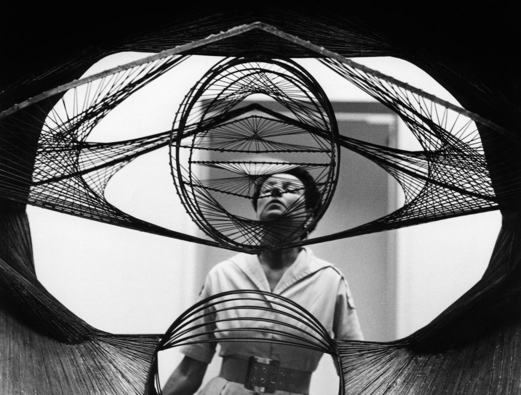 Roloff Beny fotografierte Peggy Guggenheim auf der Biennale in Venedig durch die Skulptur Developable Surface des Künstlers Antoine Pevsner hindurch. © Roloff Beny / Courtesy of National Archives of Canada