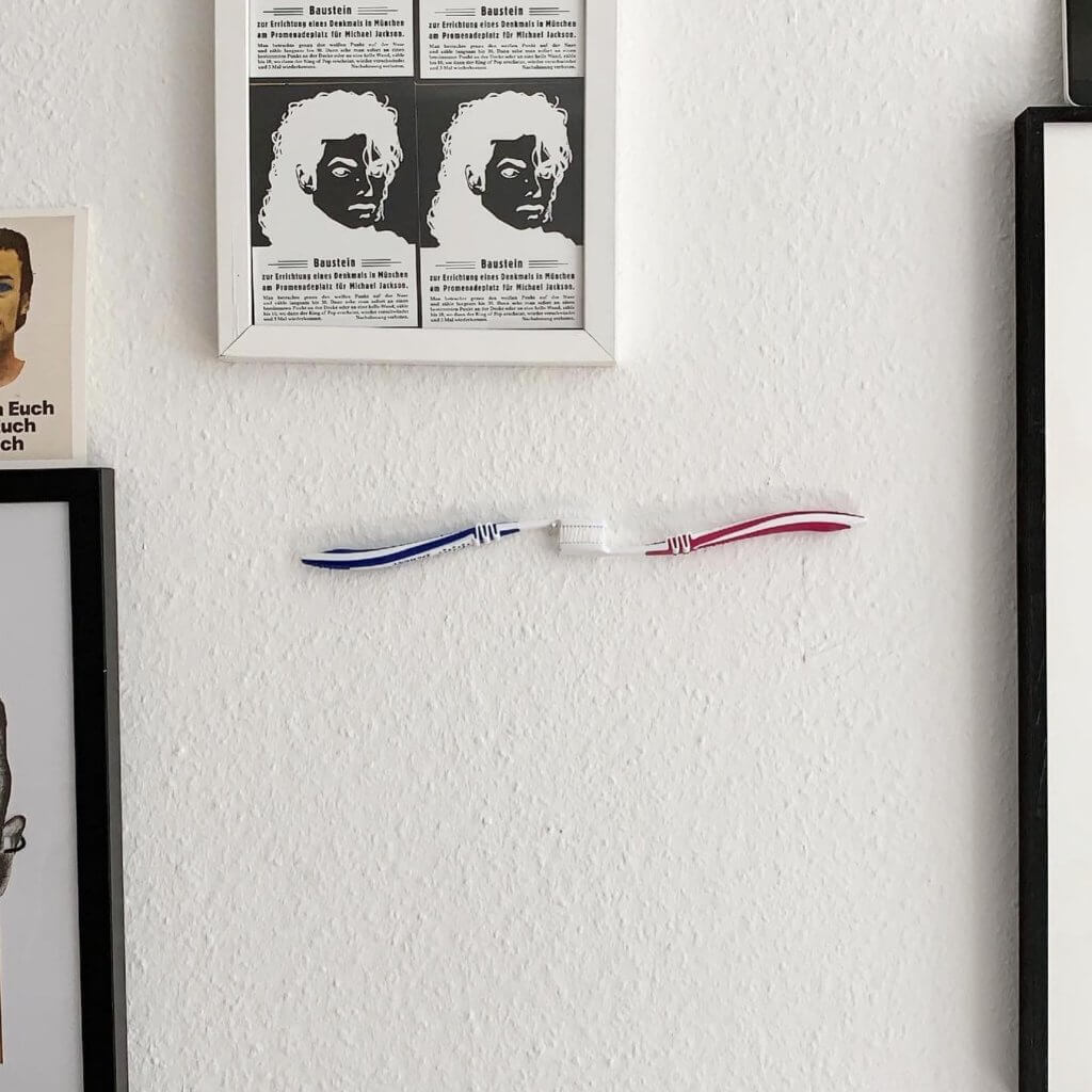 Die Zahnbürsten-Arbeit "L’amour dure 3 minutes" von Milen Till hängt zwischen anderen Kunstwerken an einer weißen Wand.