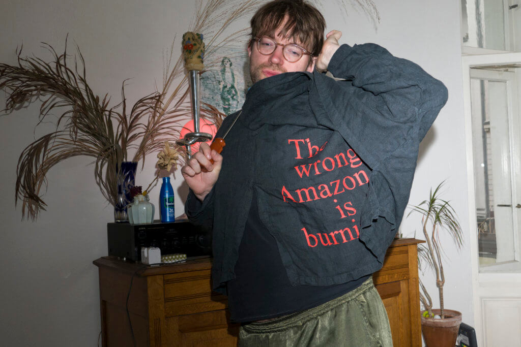 Jacke aus der Merch-Kollektion von "Arts of the Working Class". Das Kleidungsstück ist schwarz, darauf steht "The wrong Amazon is burning".