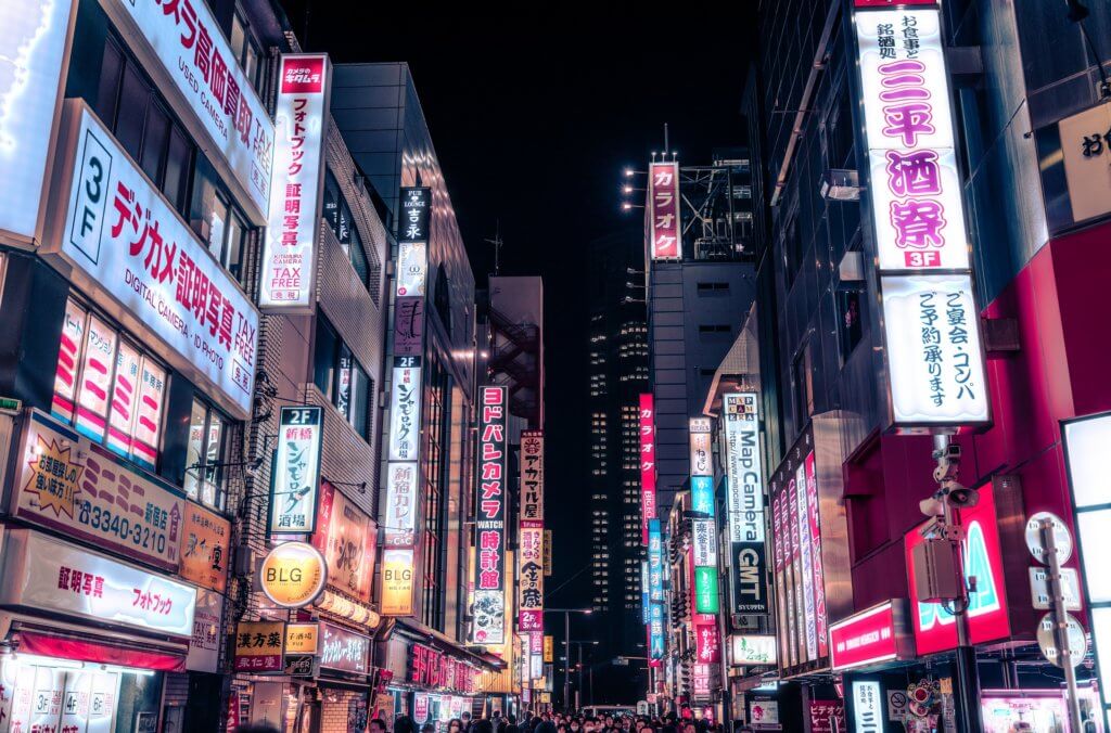 Tokios Stadtteil Shinjuku bei Dunkelheit. Links und rechts der vollen Straße überall Leuchtreklame.