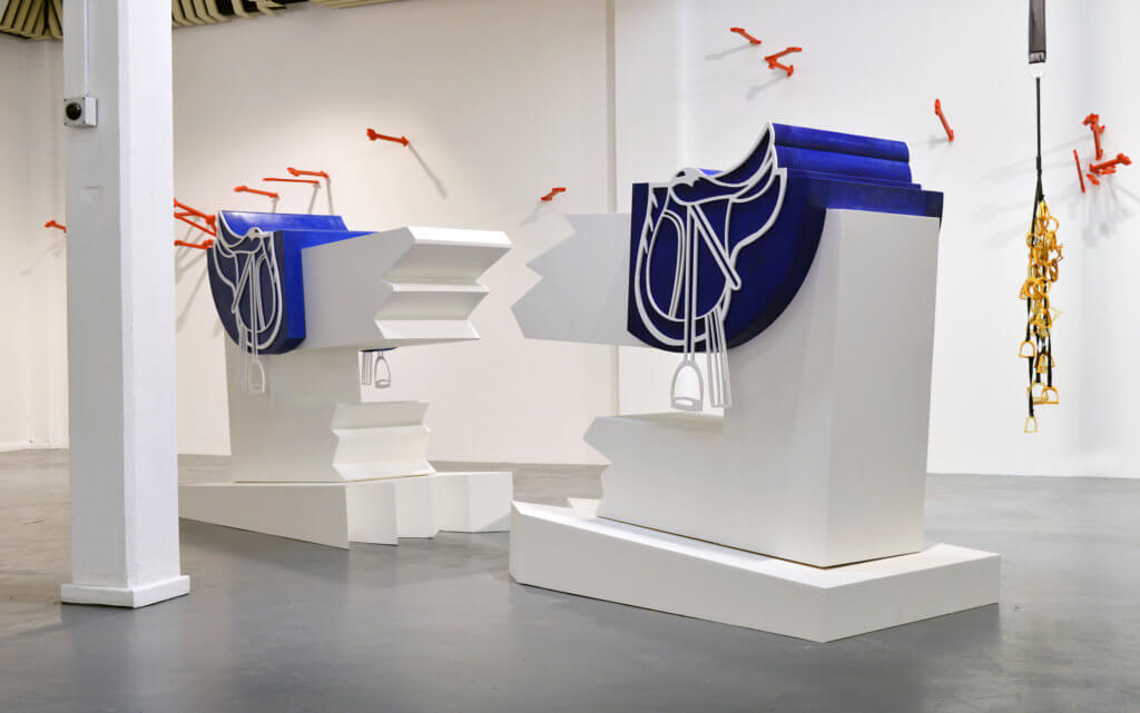 Installationsansicht einer Ausstellung von Liam Fallon. Mittig im Bild die Skulptur "La Saudade", bestehen unter anderem aus zwei stilisierten Satteln.