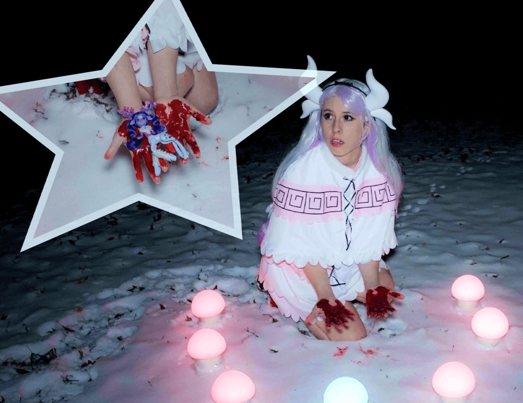 Die Künstlerin Emma Pryde. Auf dem Foto sitzt sie mit lilafarbener Perücke und einem Hörner-Haarreif im Schnee. Ihre Hände sind rot beschmiert, sie hält eine Fantasiefigur.