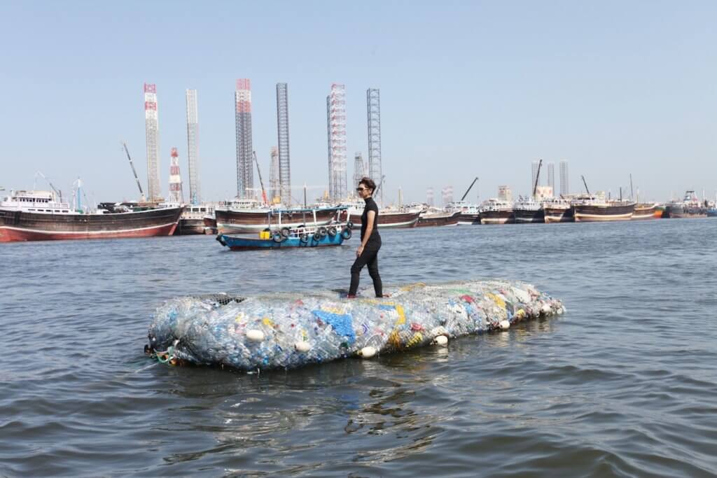 Die Künstlerin Tita Salina steht auf einer Insel aus Müll, die im Wasser eines Hafens treibt.
