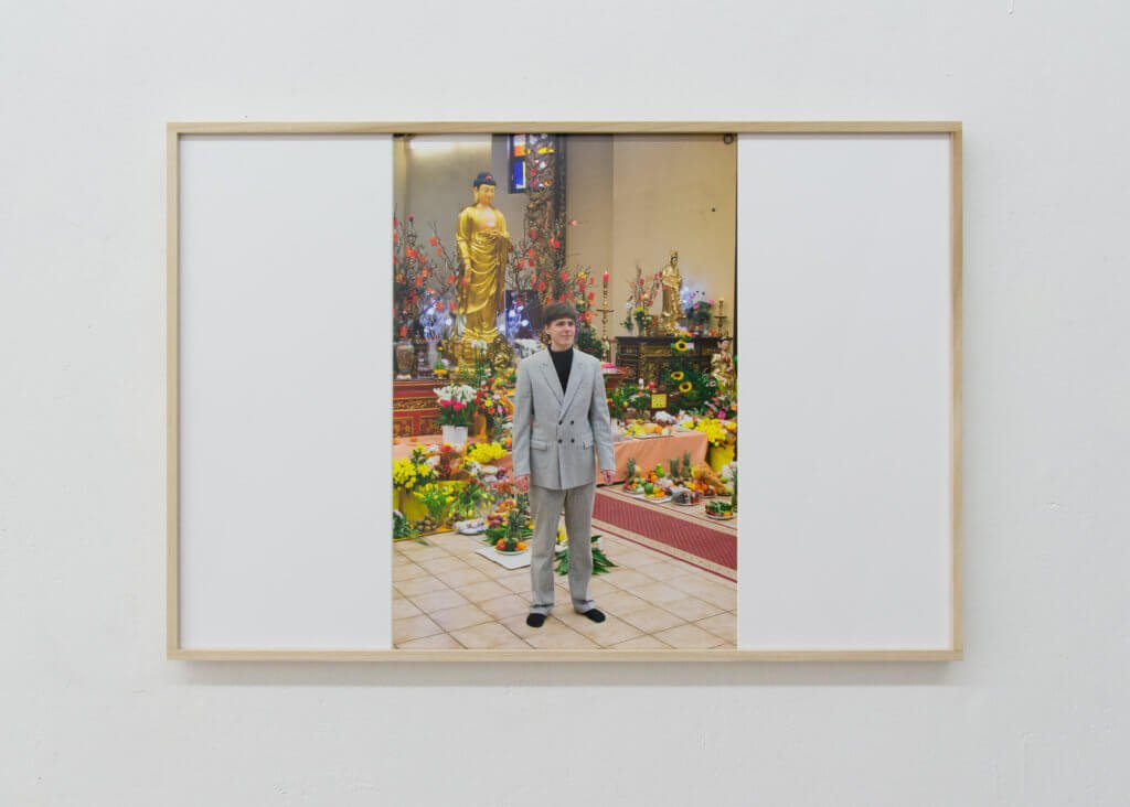 Fotografie von Niklas Taleb zeigt einen Mann im grauen Anzug vor Blumen und einer Buddha-Statue.