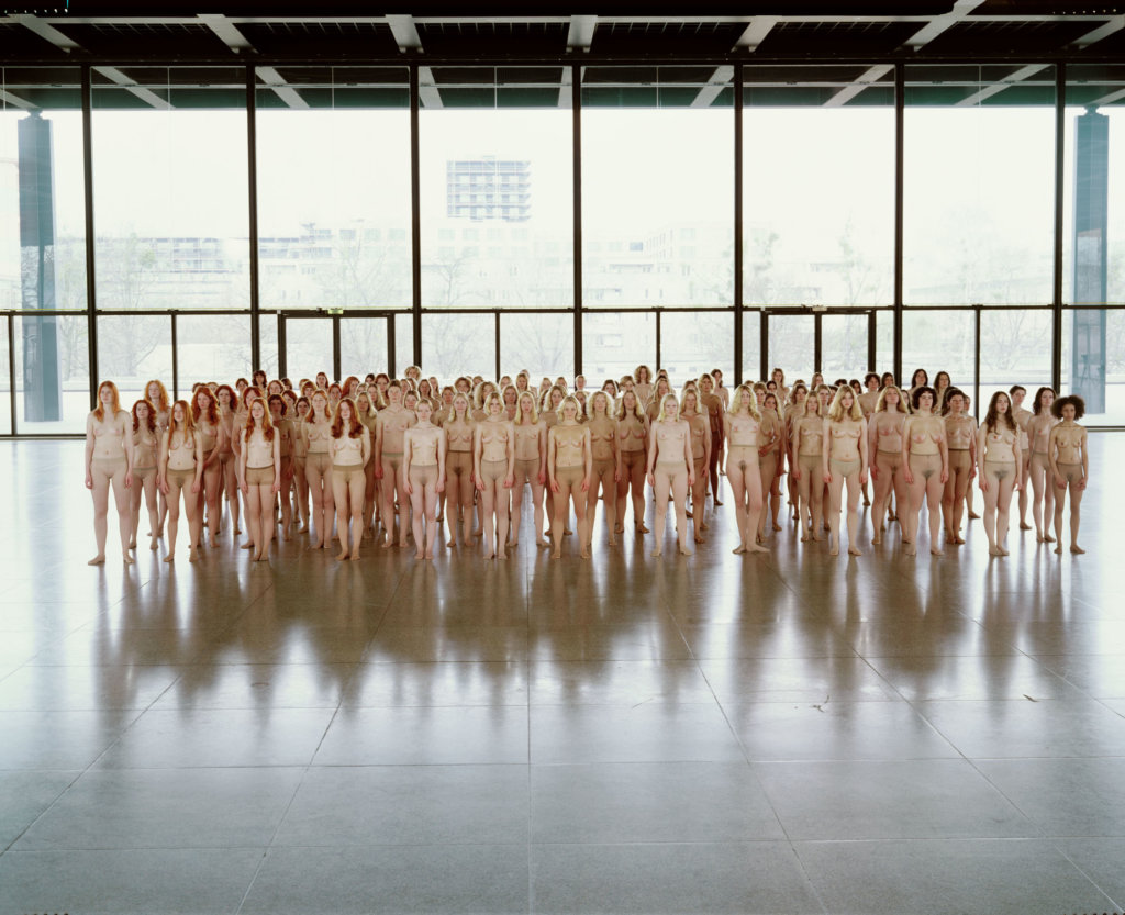 Viele Frauen stehen nur mit einer hautfarbenen Strumpfhose bekleidet nebeneinander für eine Installation von Vanessa Beecroft.