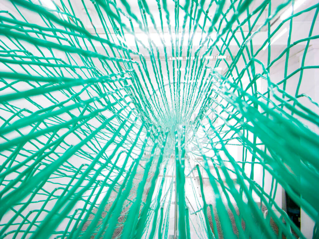 Blick durch ein filigranes Netz in einen Galerieraum.