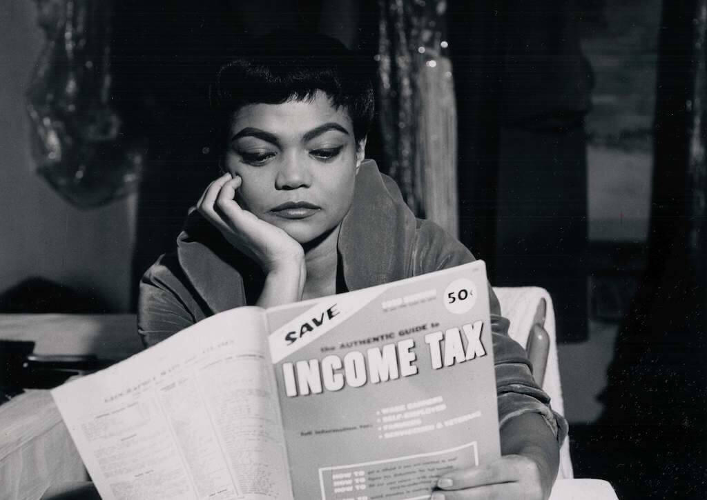Man sieht eine afroamerikanische Frau lesend. Sie beschäftigt sich mit der Einkommenssteuer. 