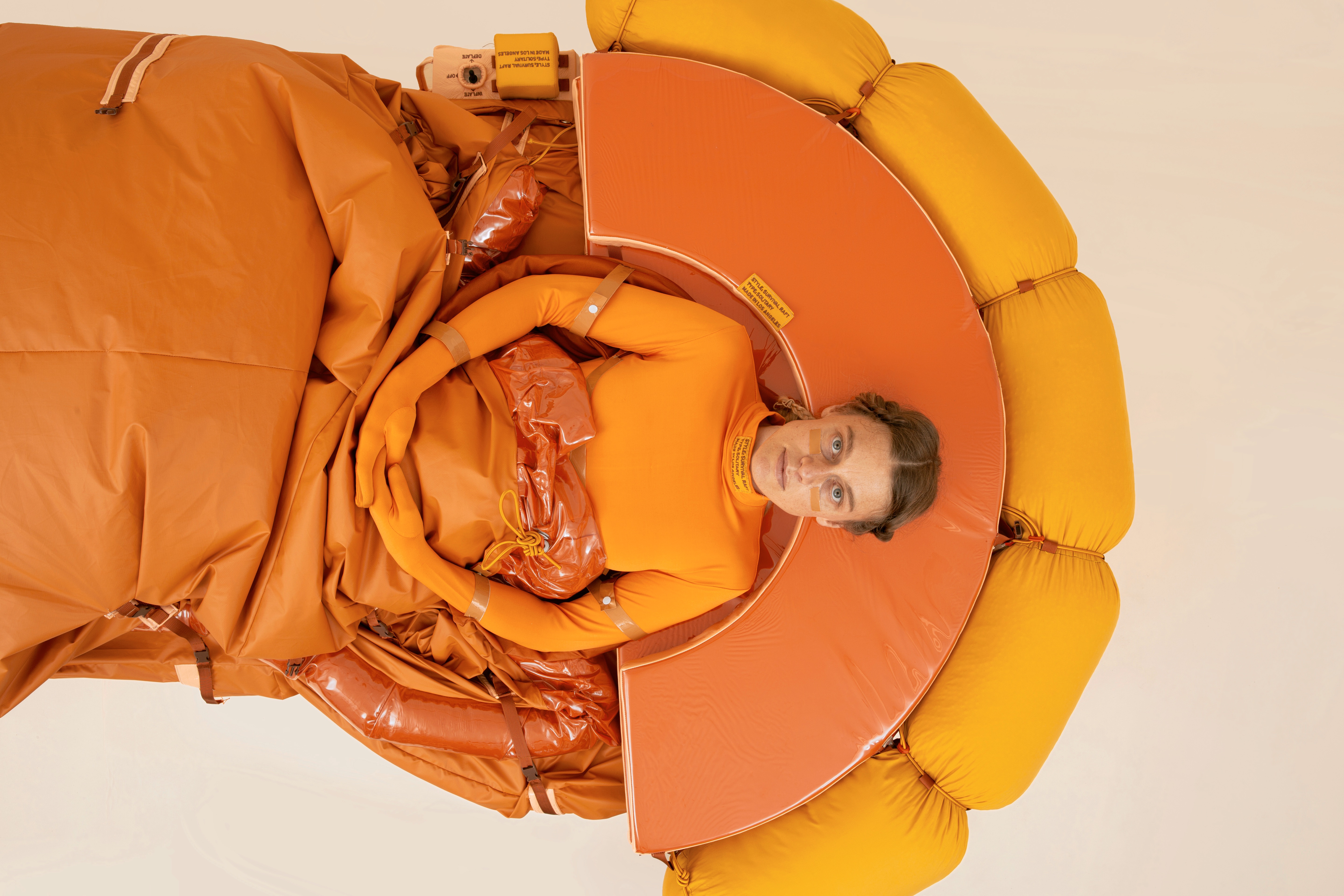 Lucy McRae liegt in ihrer Arbeit "Solitary Survival Raft", eine Art orangefarbenes Rettungsboot.