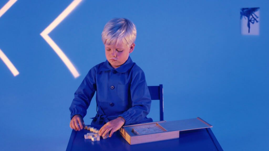 Ein blonder Junge sitzt in einem blauen Zimmer und spielt ein Spiel