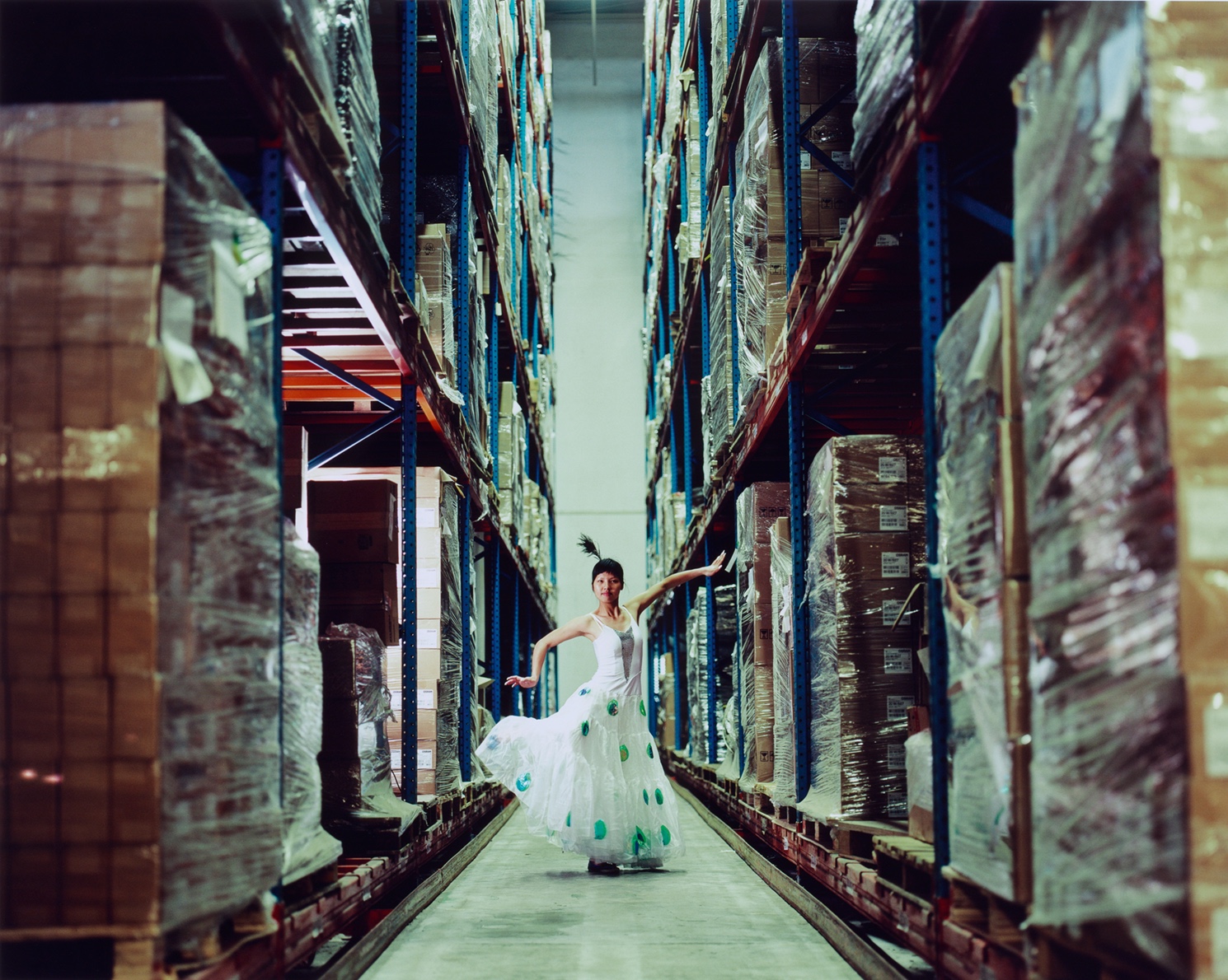 Eine Frau tanzt in langem Kleid und mit Federschmuck im Haar in einer Fabrikhalle.