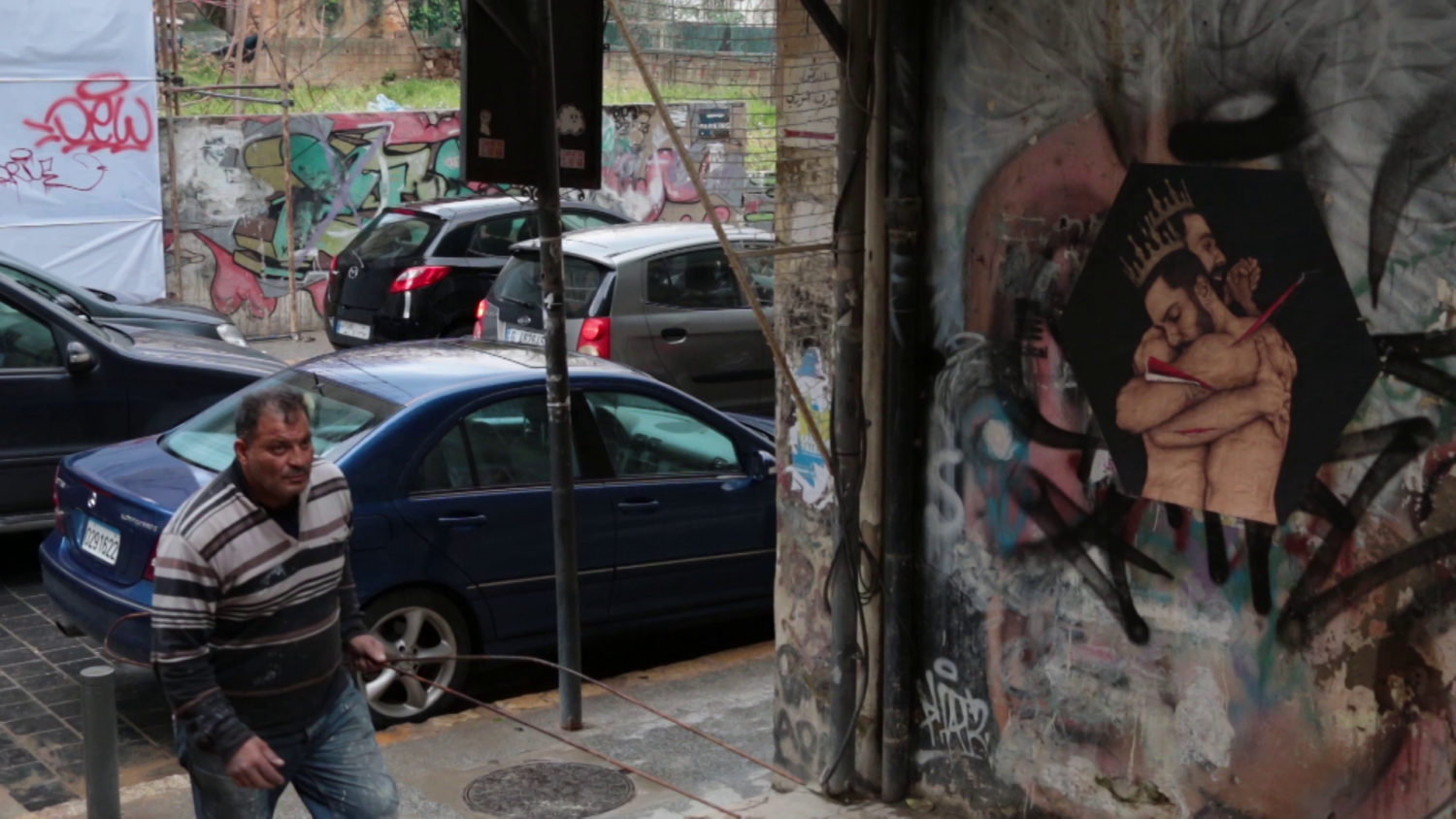 Ein Mann geht in eine Seitenstraße. An der Wand ist eine Zeichnung von zwei Männern mit freiem Oberkörper, die einander im Arm halten.