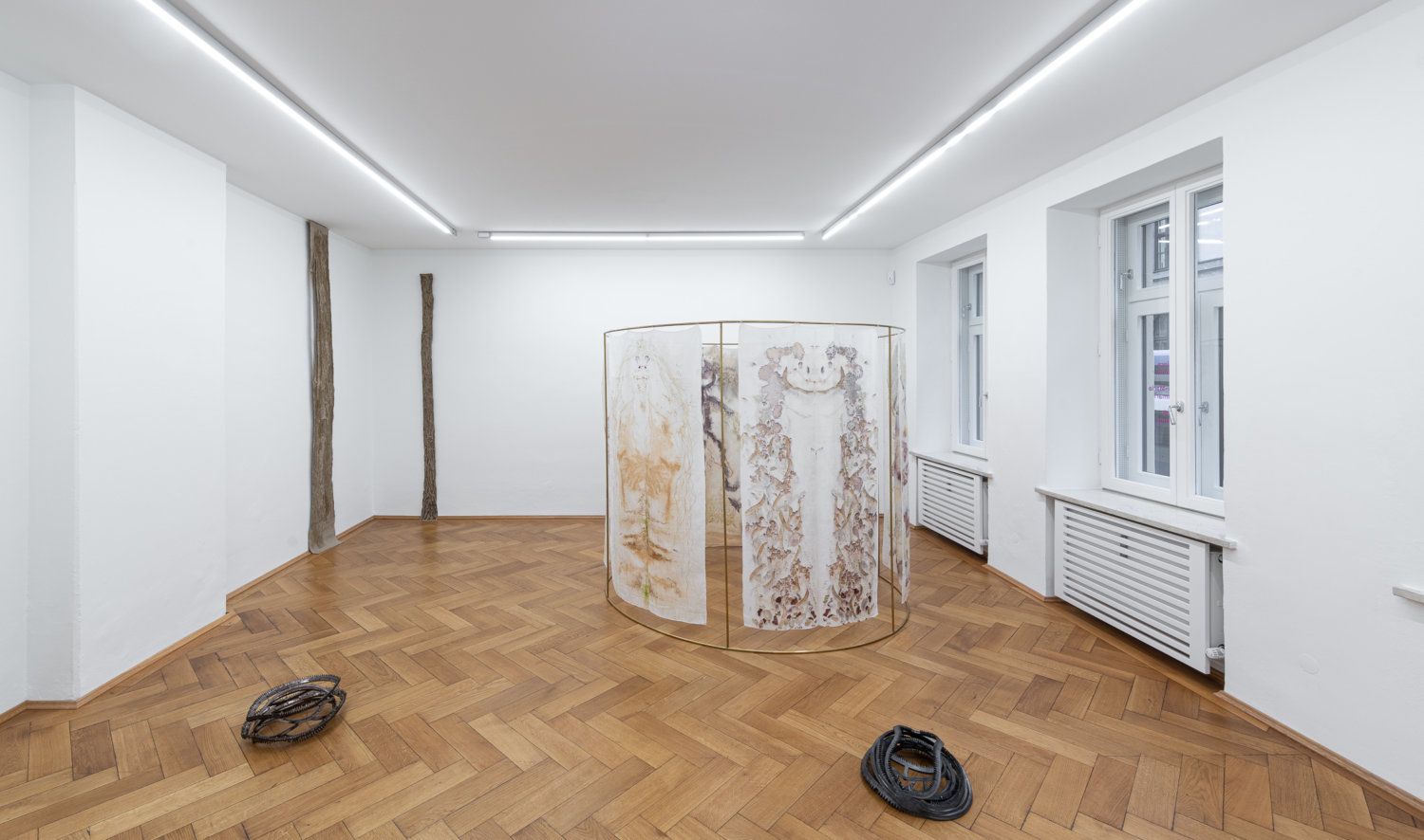 Installationsansicht der Ausstellung "On Survival". An der Wand zwei Skulpturen von Helene Appel, auf dem Boden zwei Fallen-artige Skulpturen von Hanna-Maria Hammari. Außerdem steht im Raum eine Skulptur mit Stoffbahnen von Chiara Camoni.