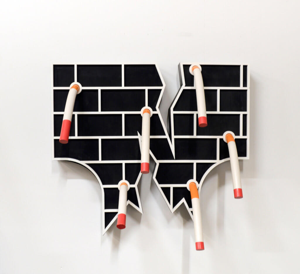 Die Skulptur "Blowback" von Liam Fallon, eine schwarze Backsteinwand, aus der Zigaretten hängen.