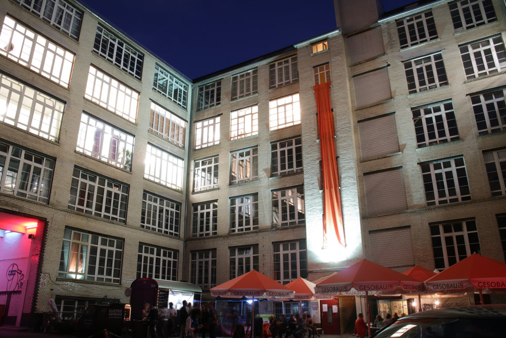 Kunst in den Gerichtshöfen in Berlin Wedding. Beleuchtete Häuserfassade mit herunterhängendem Stoff in Orange. Einige Sonnenschirme. 