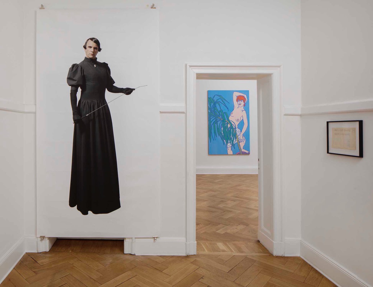 Eingangssituation in einer Berliner Altbauwohnung. Zu sehen ist der Künstler Björn Melhus als Ayn Rand. Im Hintergrund ein Bild von Otto Muehl mit einer Nacktdarstellung einer Frau. 