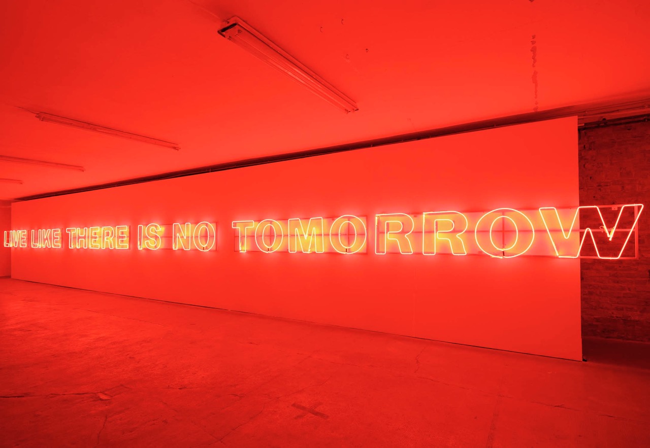 Kellerraum mit Neonröhren an der Wand, die den Raum in rotes Licht tauchen. Dort steht: Live like there is no tomorrow. 