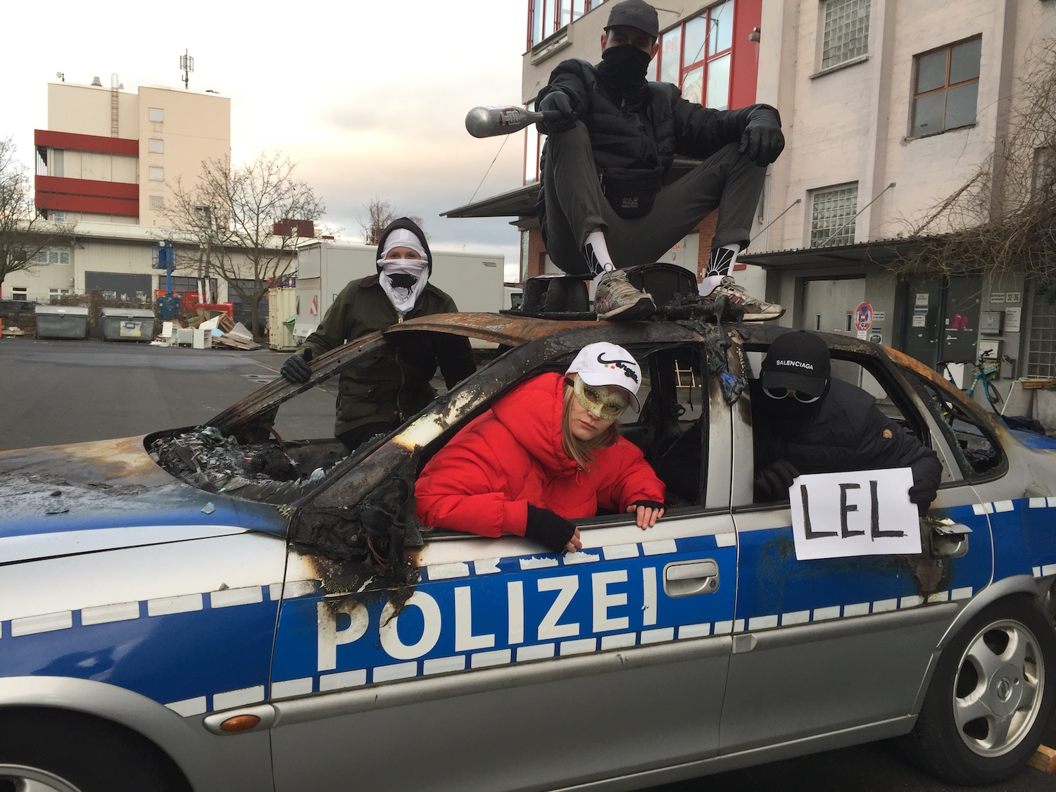 Die Frankfurter Hauptschule posiert mit einem ausgebrannten Polizeiauto. Ein Mitglied der Gruppe hält einen Zettel mit der Aufschrift "lel".