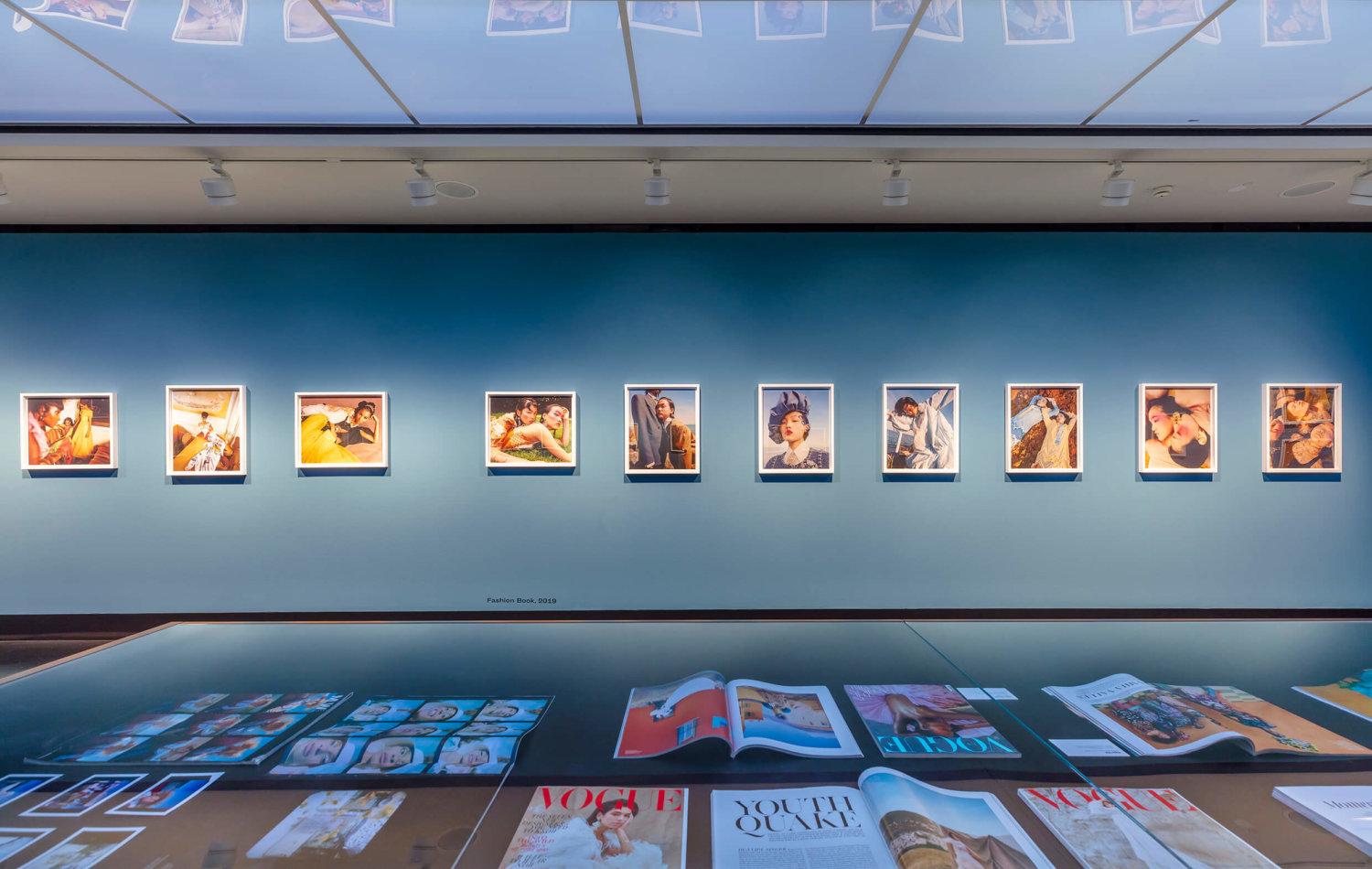 Blaue Ausstellungswand mit gerahmten Modefotografien von Nadine Ijewere, im Vordergrund eine Glasvitrine mit Modemagazinen