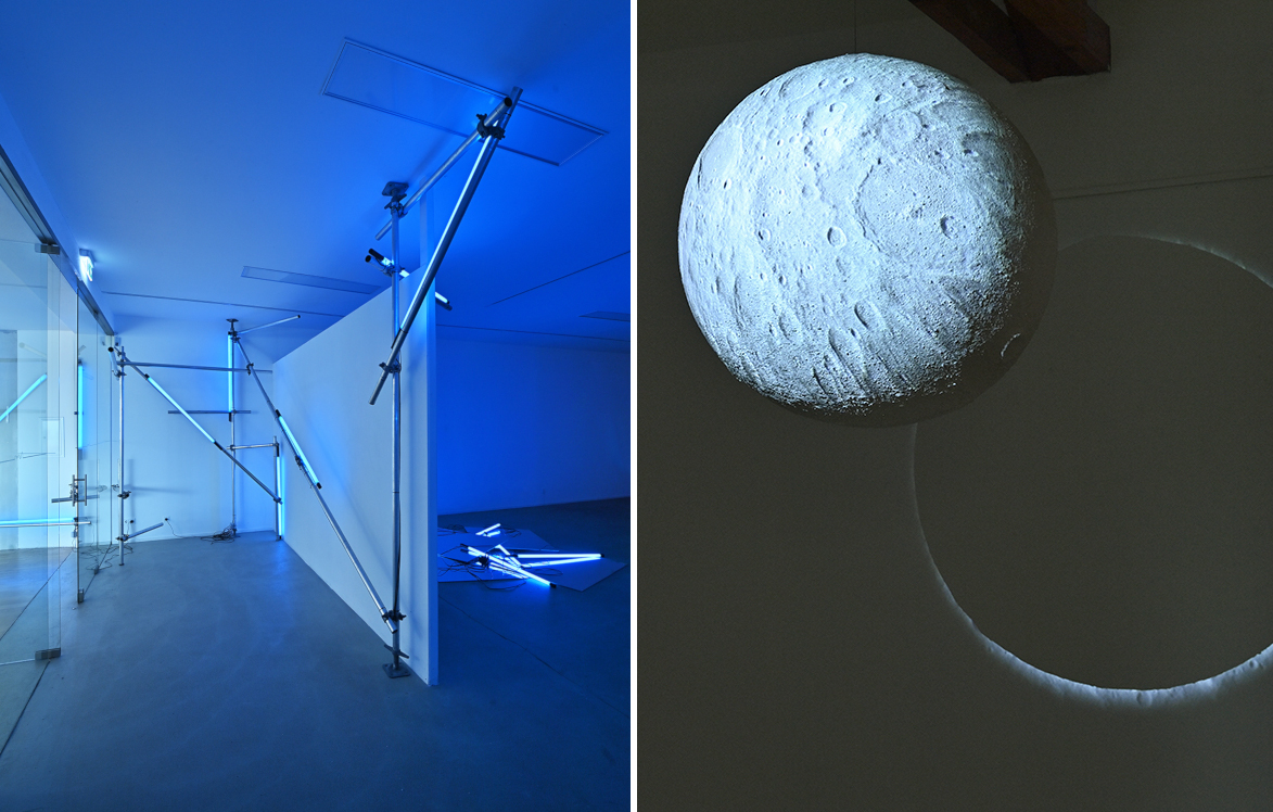 Links eine Installation von blauen Neonröhren quer durch den Raum, rechts eine Mondkugel, die einen Schatten an die Wand wirft.