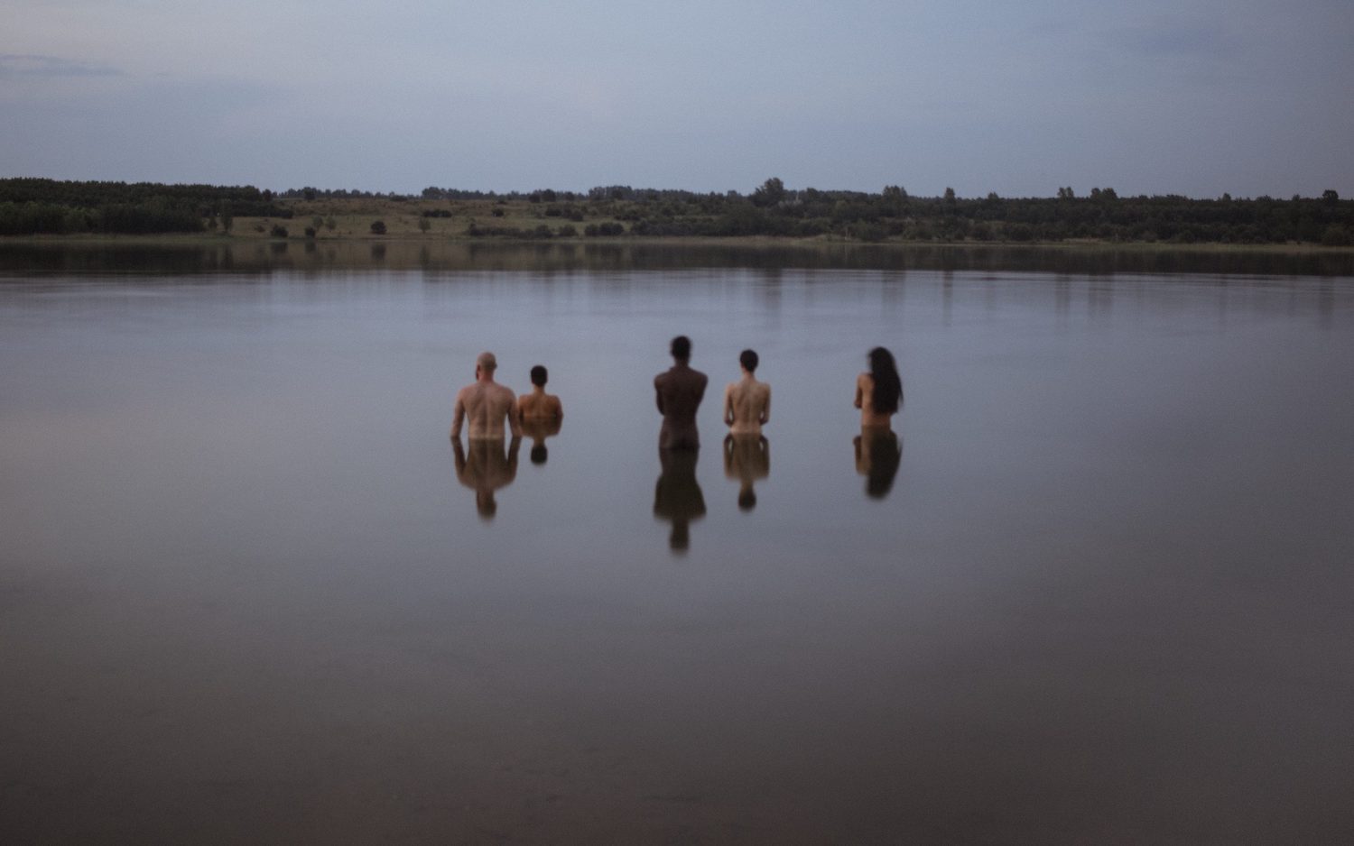 Fünf Personen stehen nackt im Wasser. Sie sind von hinten zu sehen.