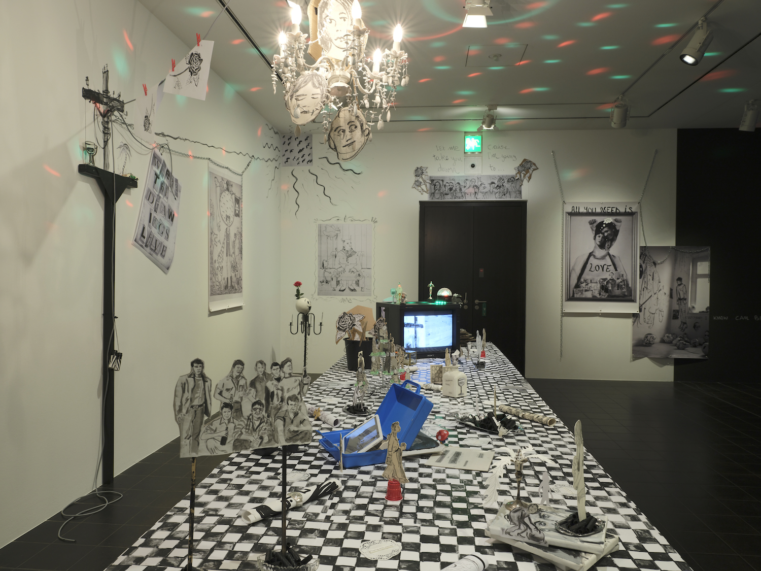 Installation von Serena Ferrario mit Schwarz-Weiß-Zeichnungen auf Schachbrettmuster und einem Kronleuchter an der Decke.
