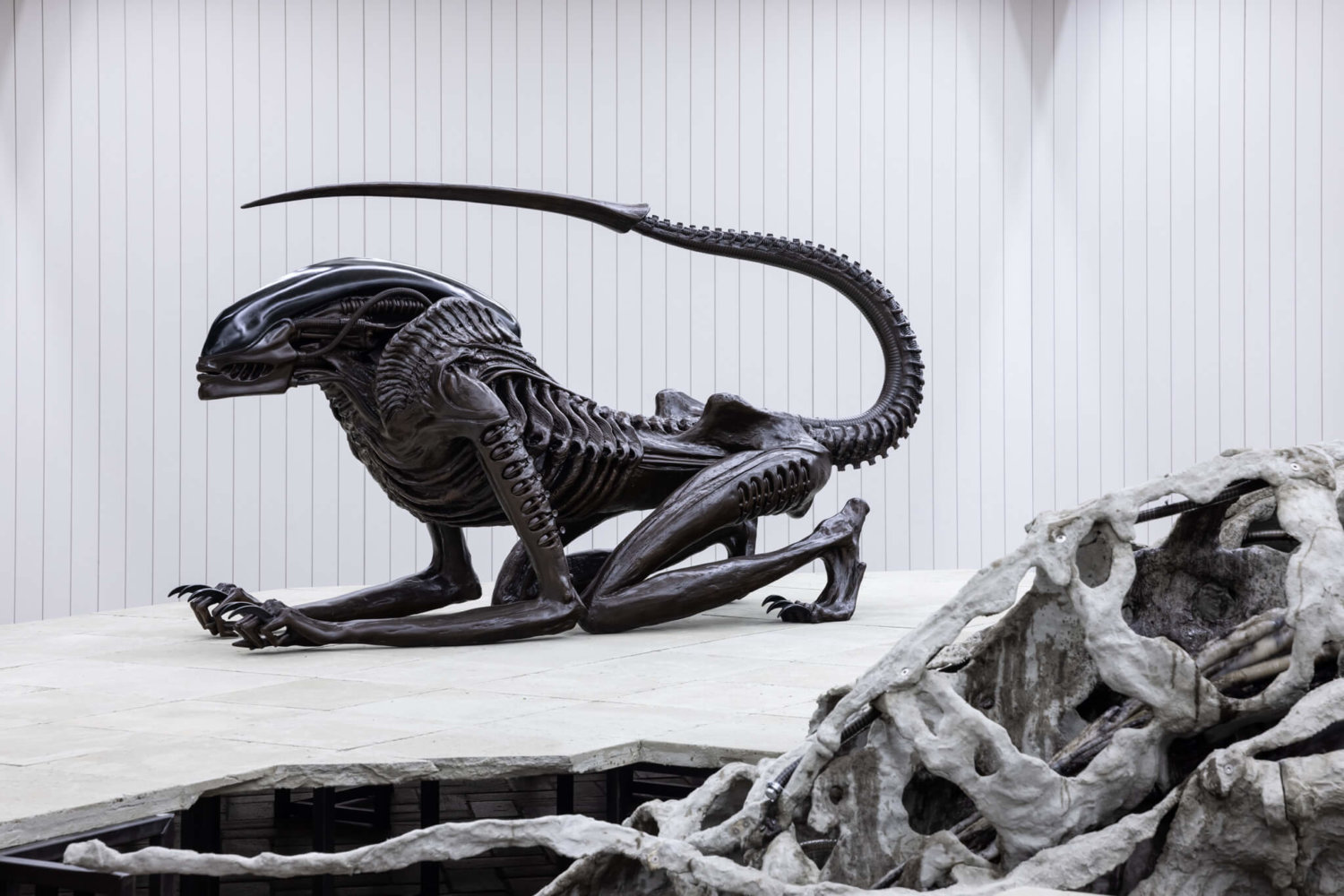 Auf einem Podest ruht die alienhafte Skulptur "Necronom" von HR Giger wie eine skeletthafte Katze.