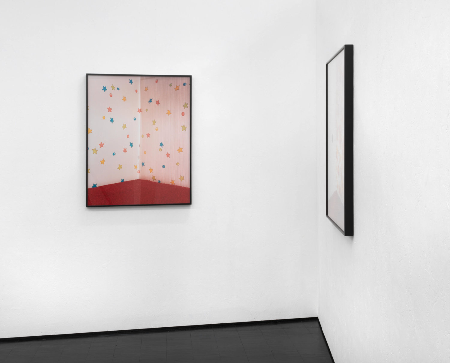Zwei Fotografien an weißen Ausstellungswänden, frontal zu sehen ist ein Foto von einer Raumecke mit einer Sternen-Tapete und rotem Teppichboden