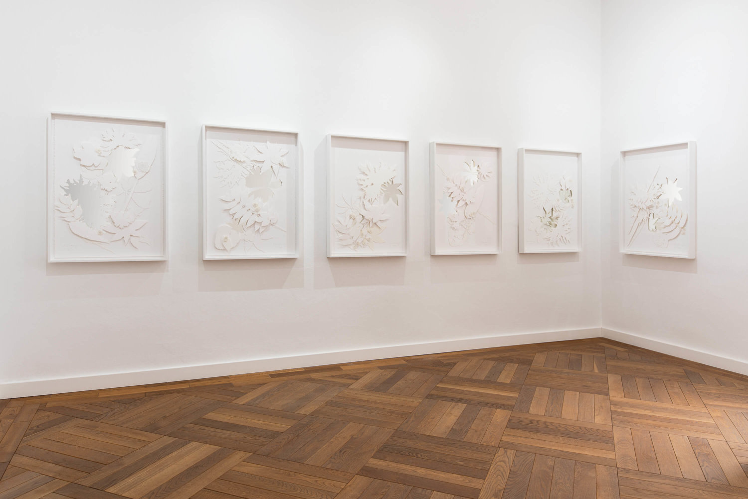 Filigrane Papier-Kunstwerke mit Blättern und Blüten, die auf Spiegeln angebracht und eingerahmt sind, an einer weißen Wand befestigt