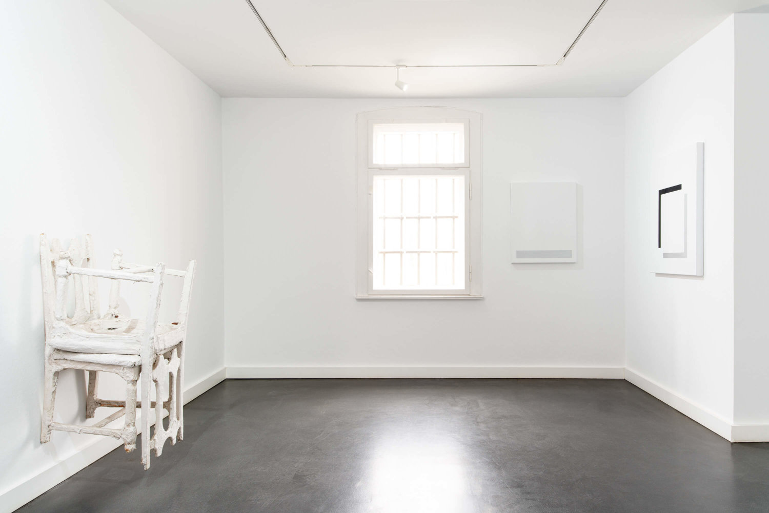 Ein weißer Ausstellungsraum, links ein Objekt aus zwei weißen Stühlen an der Wand, rechts in der Ecke zwei weitere Kunstwerke