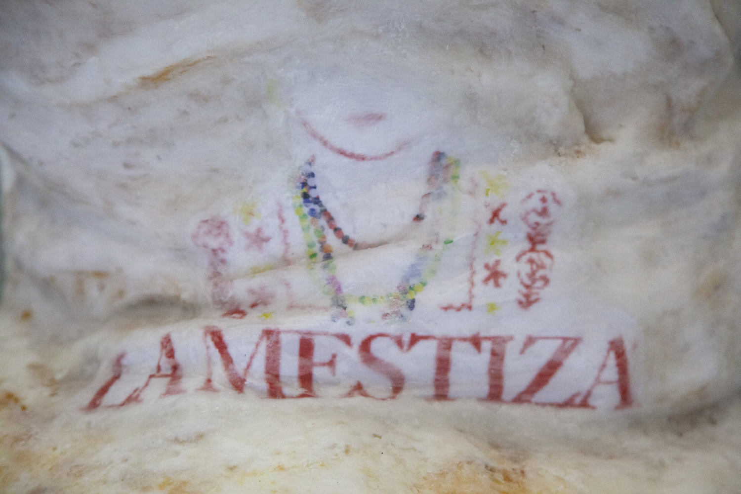 Verschwommenes Logo zeigt den Oberkörper einer bunt gekleideten Figur sowie den Schriftzug "La Mestiza".