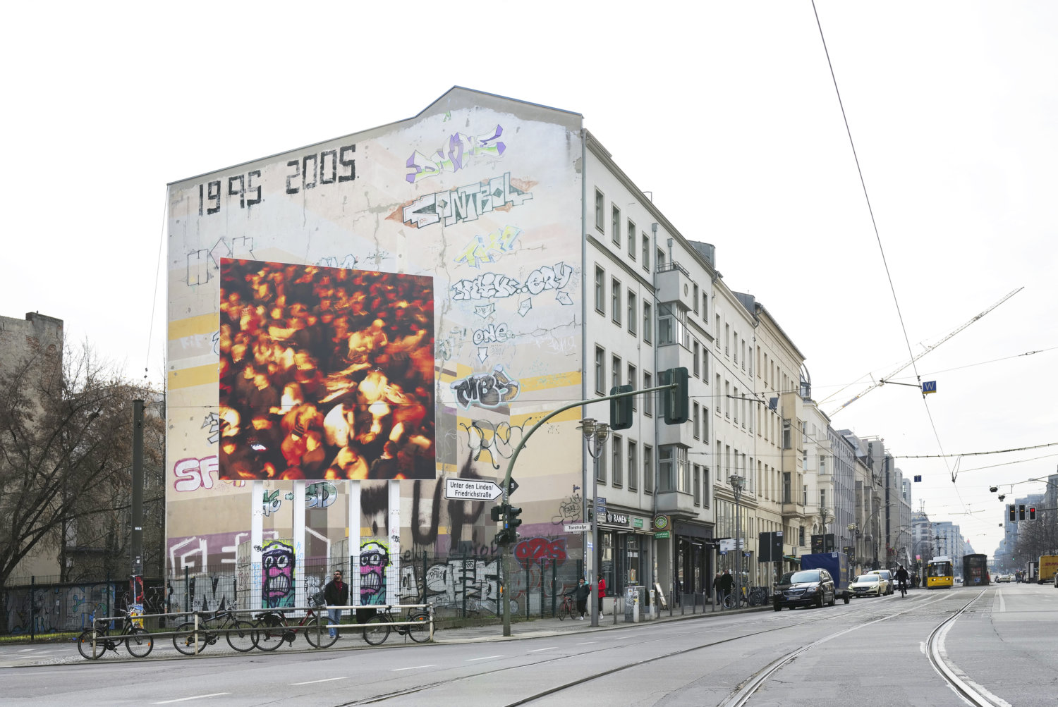 Straßenansicht in Berlin-Mitte, eine mit Graffiti besprühte Häuserfassade, vor der ein großes Bildboard einer Nan Goldin Fotografie steht
