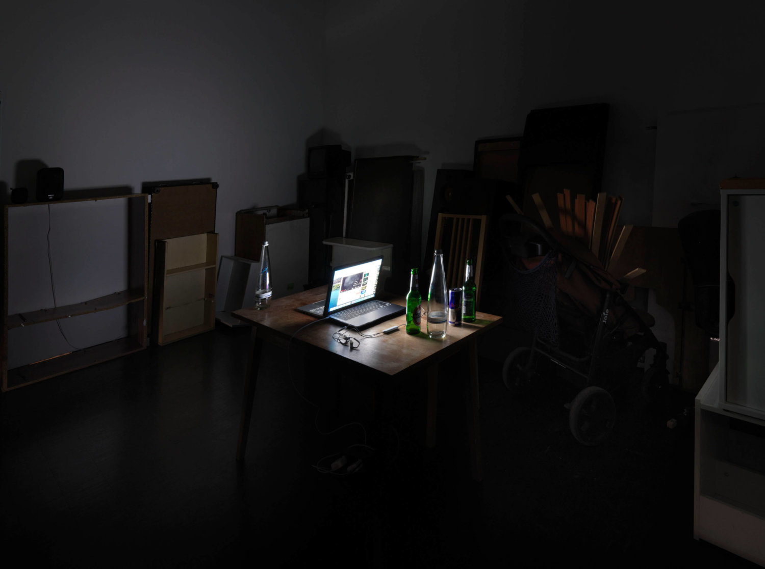 Ein dunkler Raum, der durch das Display eines Laptops erleuchtet wird, Flaschen stehen drumherum auf einem Tisch