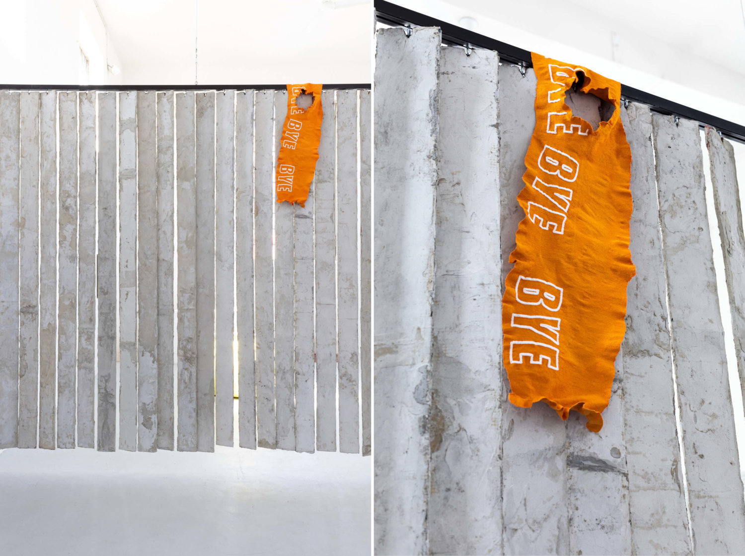 Ein industrieller Lamellen-Vorhang hängt an einer Schiene von der Decke, darüber ein orangefarbenes Stück Stoff auf dem die Wörter "Bye, Bye, Bye" zu lesen sind.