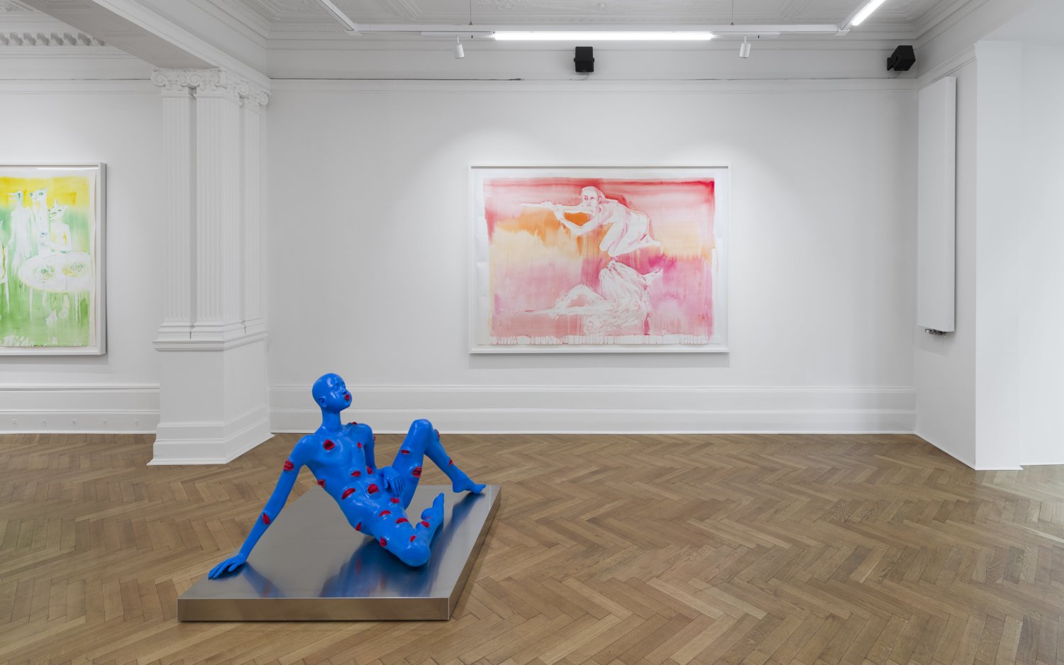 An der Wand hängen zwei große Aquarellmalereien von Marianna Simnett. Auf dem Boden steht eine Skulptur der Künstlerin, die komplett blau und mit roten Mündern überzogen ist. Sie bläht die Wangen auf.